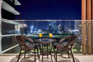 A balcony with wicker chairs and a table, overlooking a cityscape at night. - Chic Studio | Pool View Balcony | Avelon Arjan (Dubai)