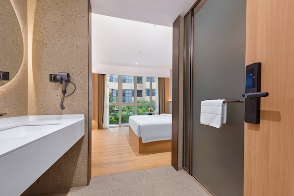 Une chambre d’hôtel avec un grand miroir, un sèche-cheveux, un lit et une vue sur un immeuble par la fenêtre.