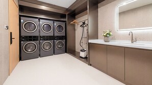 Un moderno lavadero con cuatro lavadoras, un aspirador y un lavabo con un espejo arriba.