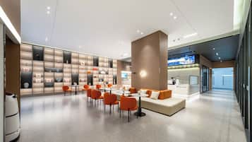 Um hall de hotel moderno com uma área de estar central, uma parede com obras de arte emolduradas e um balcão de recepção.