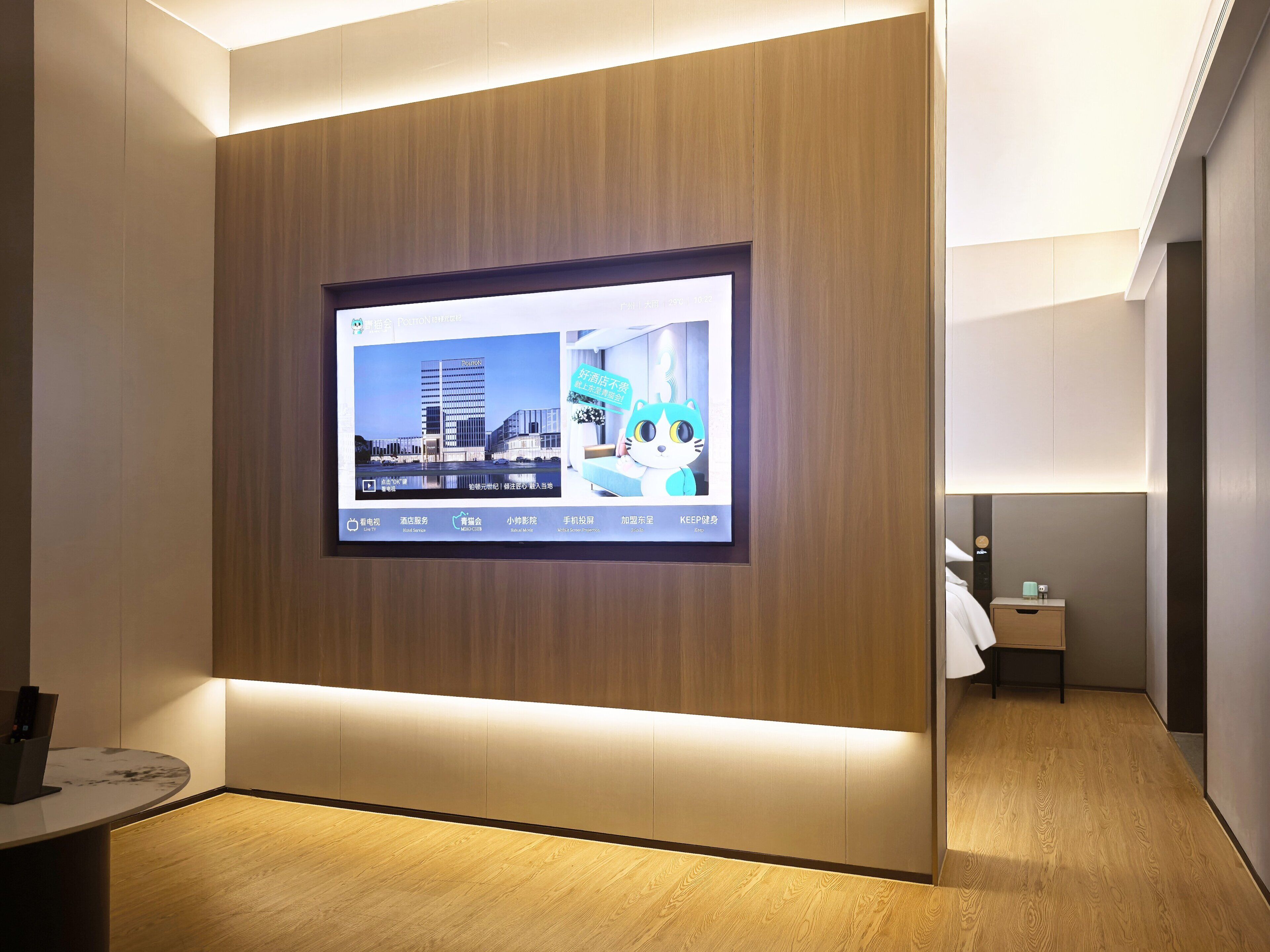 Een hotellobby met een groot digitaal scherm aan de muur, een receptiebalie en een houten vloer.