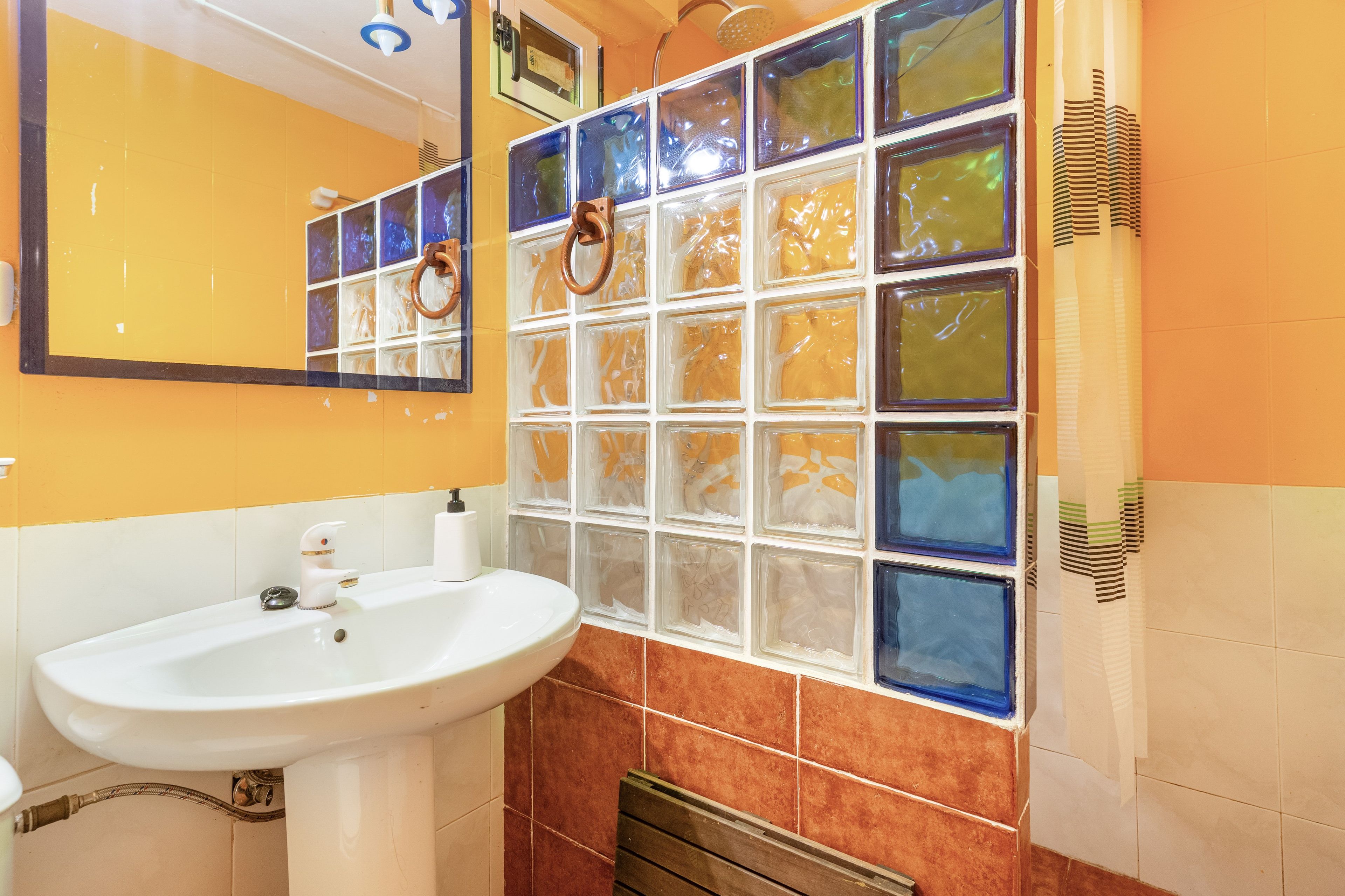 Un baño con un lavamanos blanco, un espejo y una pared de azulejos con un vitral.