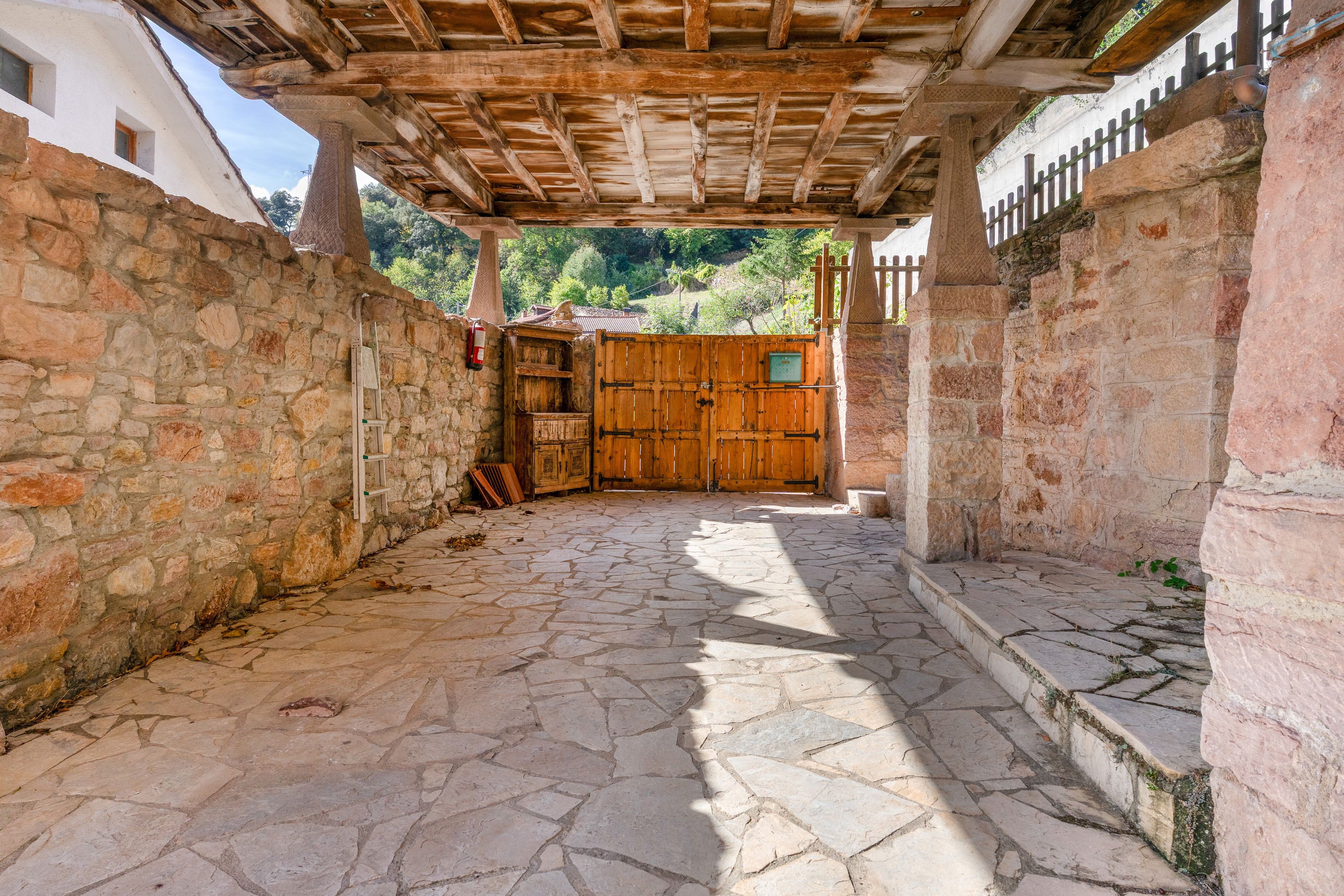 Ein von Pflastersteinen ausgelegter Innenhof mit einem hölzernen Tor, Steinmauern und einer Holzdeckenkonstruktion.