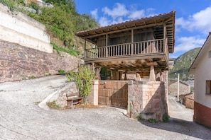 Un edificio de piedra tradicional con un balcón de madera, una verja de piedra y un camino adoquinado.