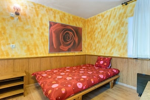 A bedroom with a wooden bed, a red and pink polka dot bedspread, a single wall-mounted light, and a large framed picture of a rose. - ‘Zentralclub La Osera’ Apartment with Mountain Views, Terrace & Shared Garden (Las Viñas)