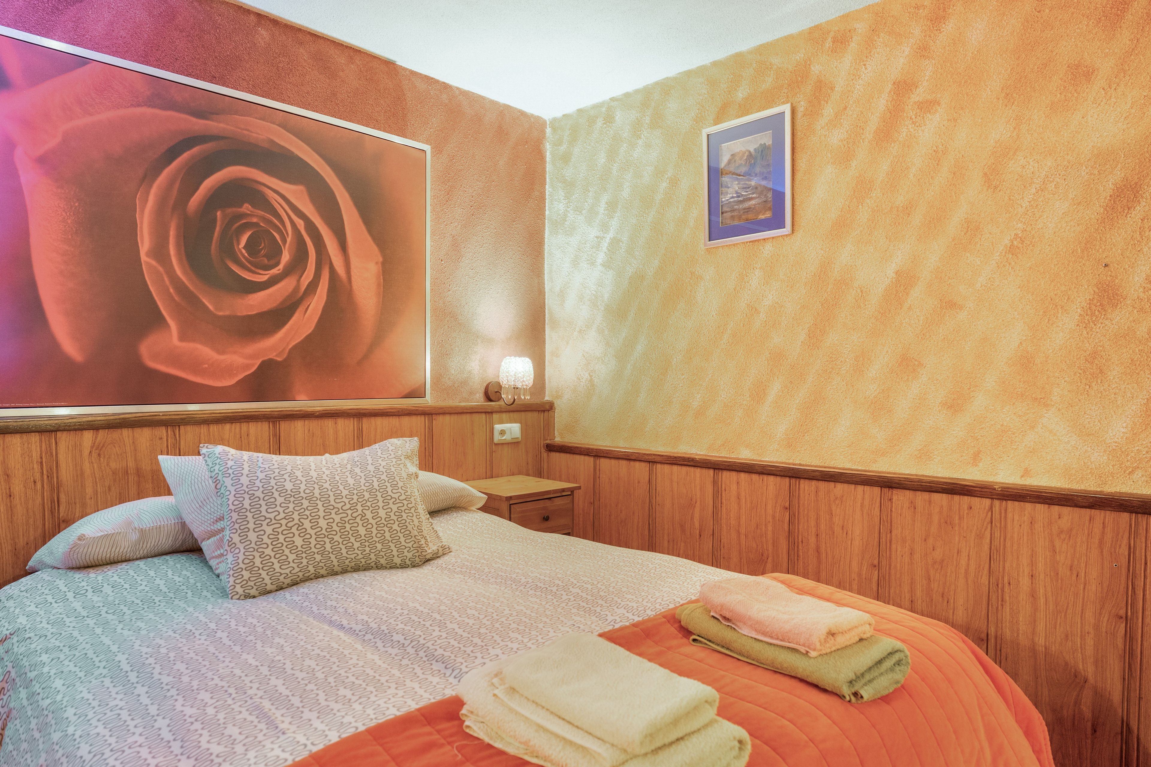 Una habitación de hotel con una cama grande, una mesita de noche, una lámpara de pared y un cuadro enmarcado.