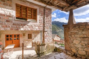 Un edificio de piedra con puerta y ventanas de madera, una escalera de piedra y vistas a montañas.