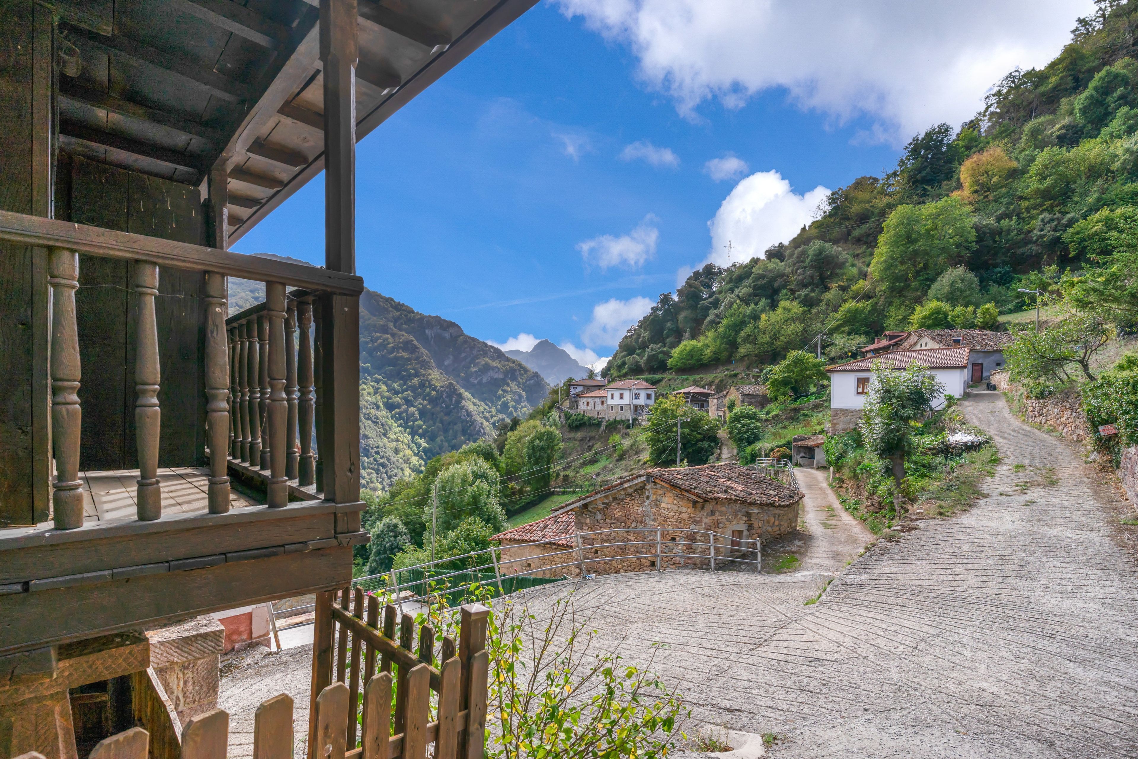 Ein Bergdorf mit traditionellen Steinhäusern, einem Kopfsteinpflasterweg und einem Holzbalkon mit Blick auf die Landschaft.