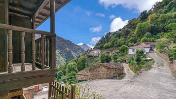 Ein Bergdorf mit traditionellen Steinhäusern, einem Kopfsteinpflasterweg und einem Holzbalkon mit Blick auf die Landschaft.