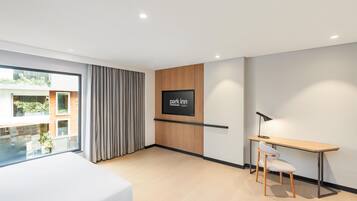 Quarto de hotel moderno com cama, escrivaninha, cadeira, televisão e vista para o exterior.