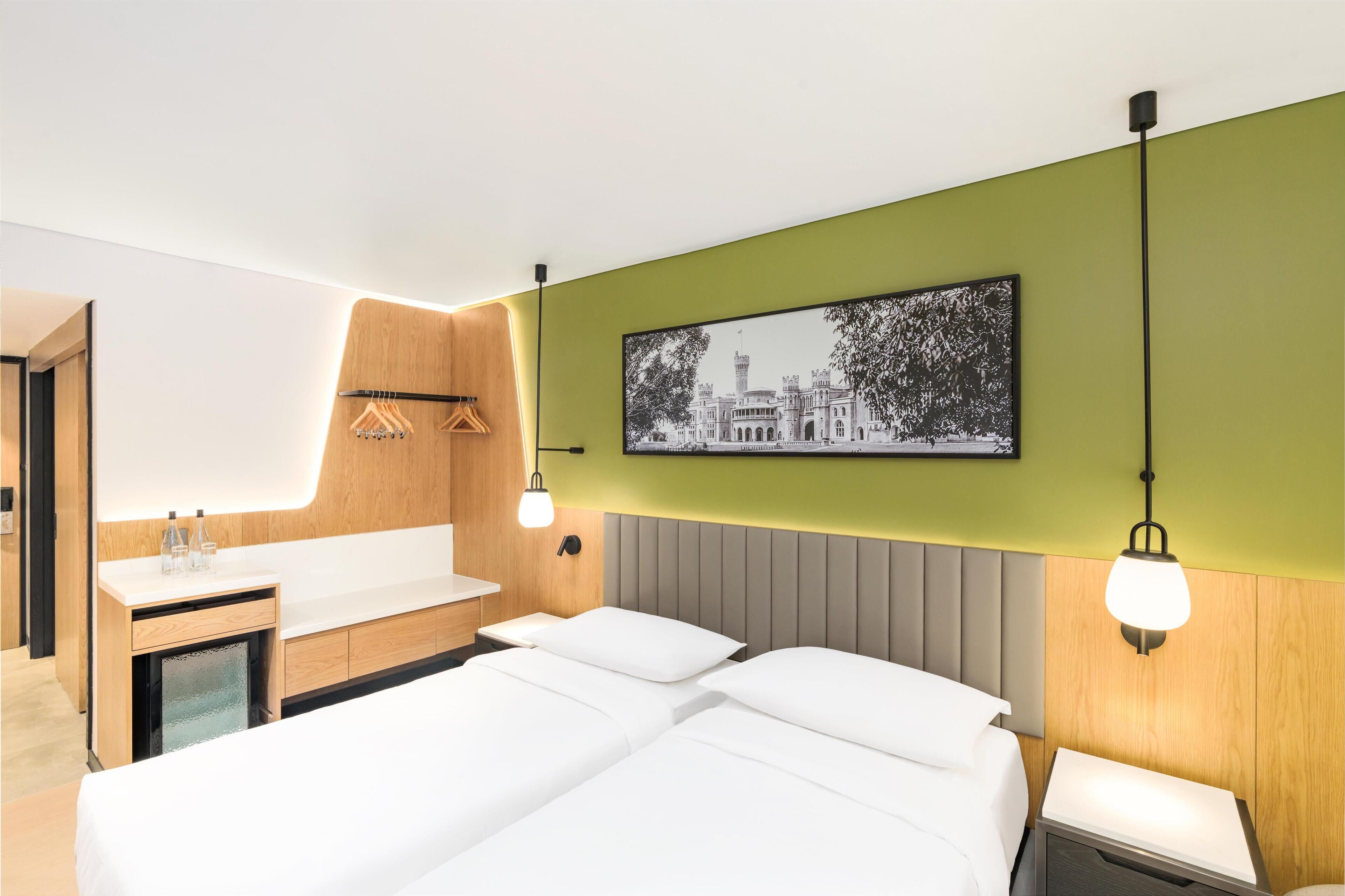 A hotel room with a bed, a bedside table, a mirror, a sink, and a wall-mounted picture.