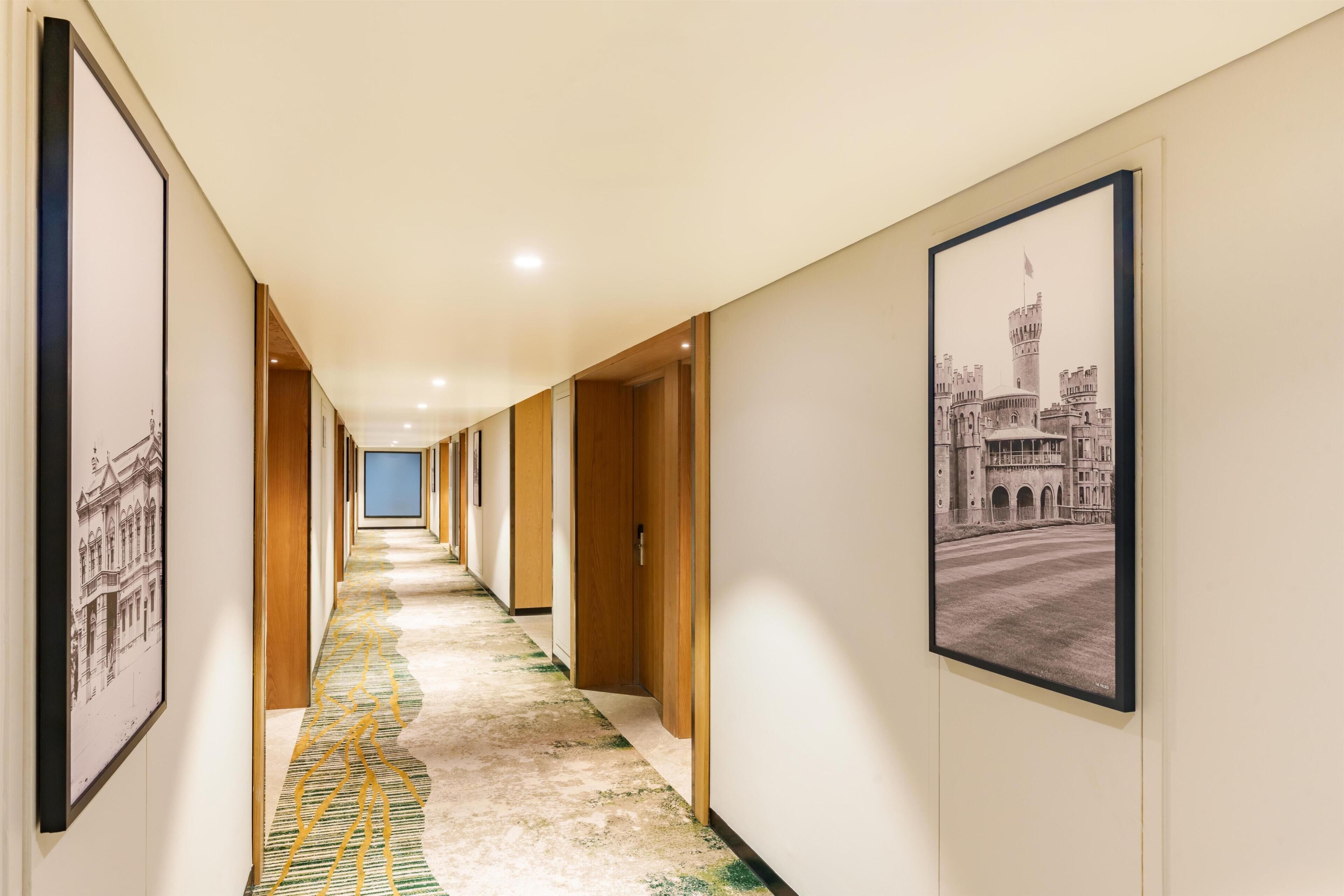 Corredor de hotel com quadros nas paredes, carpete estampado e portas de madeira.