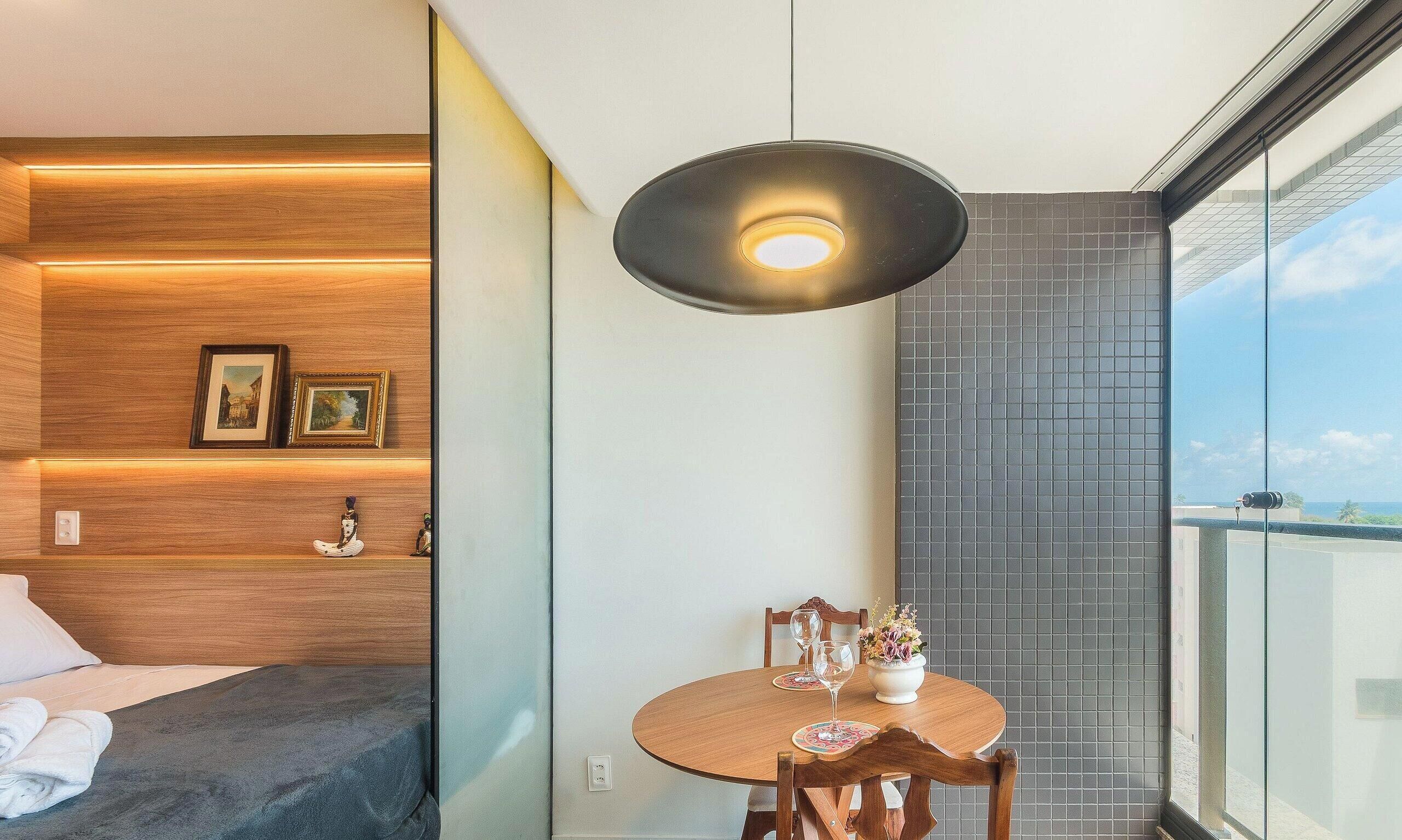 Une chambre moderne avec un lit, une table à manger et des chaises, un luminaire suspendu et une vue sur le ciel.