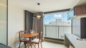 A modern dining area with a round table, four chairs, a pendant light, and a view of the city through large windows. - Studio Near the Beach in Condo w/ Pool Edf0207 (Salvador)