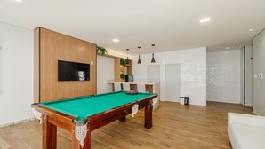 A pool table in a room with a wooden accent wall, a flat-screen TV, and a white brick wall. - Studio Near the Beach in Condo w/ Pool Edf0207 (Salvador)