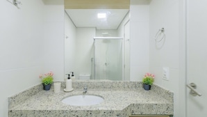 Un baño con encimera de granito, un lavabo, un espejo, ducha y dos plantas en macetas.