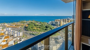 Un edificio alto con balcón que ofrece vistas a una ciudad costera, incluyendo el mar y edificios urbanos.