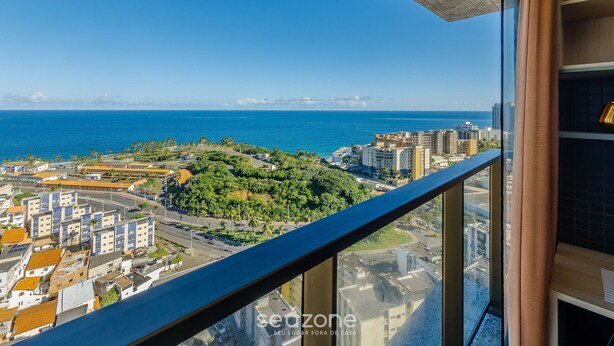 Un edificio alto con balcón que ofrece vistas a una ciudad costera, incluyendo el mar y edificios urbanos.