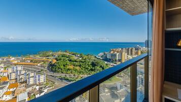 Um edifício alto com varanda e vista para a paisagem urbana costeira, incluindo o mar e edifícios.
