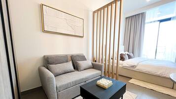 Une chambre moderne avec un canapé gris, une table basse noire et un lit recouvert d’une couette blanche.