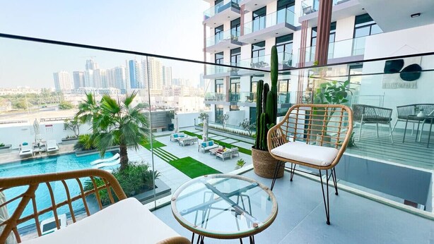 Uma varanda com mesa e cadeiras de vidro, uma piscina e vista para a cidade.