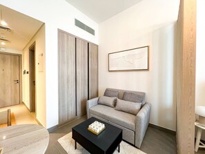 A modern living room with a grey sofa, a black coffee table, and a framed abstract artwork on the wall. - Modern Studio in JVC | Pool, Gym & BBQ Access (Dubai)