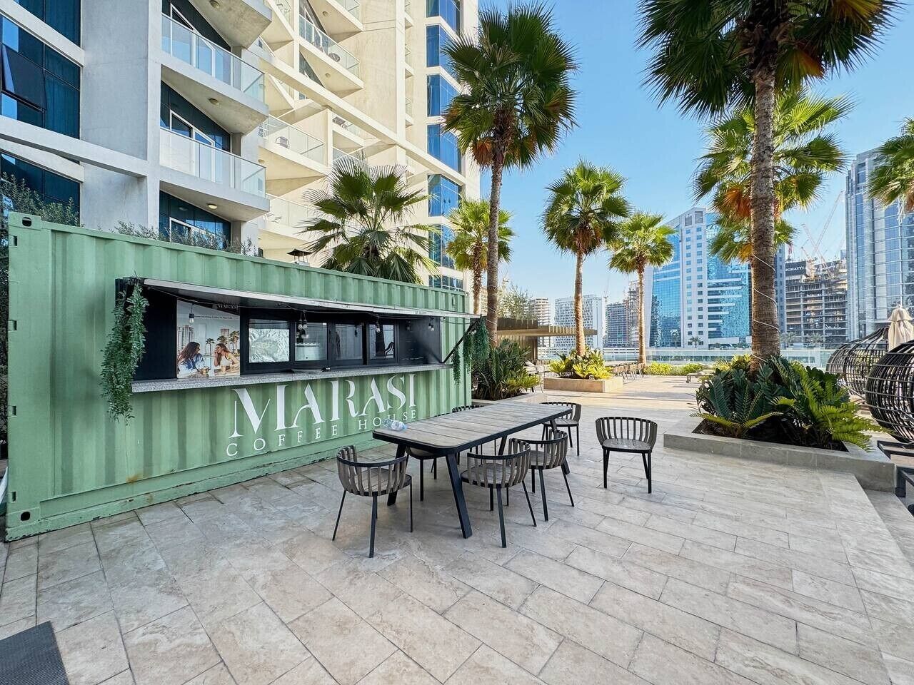 A modern outdoor seating area with a green container labeled 'MARASI COFFEE HOUSE' and a table with chairs.