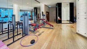 A gym with exercise equipment, a mirror wall, and a wooden floor. - Canal View Suite | DAMAC Maison Privé | 4 Guests (Dubai)