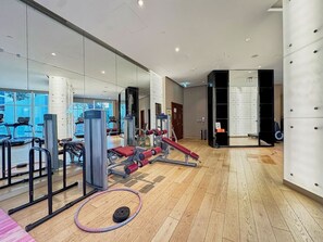 Ein Fitnessraum mit Trainingsgeräten, einer Spiegelwand und Holzboden.