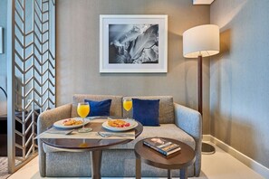 A hotel room with a sofa, two dining tables, a lamp, and a framed picture on the wall. - Canal View Suite | DAMAC Maison Privé | 4 Guests (Dubai)
