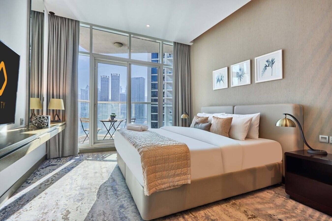 Ein modernes Hotelzimmer mit einem großen Bett, einem Schreibtisch mit Fernseher, einem Balkon mit Stadtblick und Kunstwerken an der Wand.