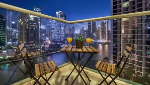 A balcony with a table and chairs, overlooking a cityscape at night. - Canal View Suite | DAMAC Maison Privé | 4 Guests (Dubai)