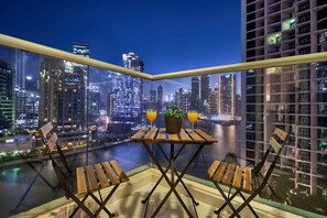 Ein Balkon mit Tisch und Stühlen, der auf eine beleuchtete Stadtlandschaft blickt.