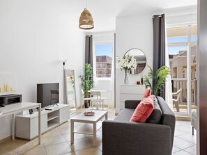 Ein modernes Wohnzimmer mit einer Couch, einem Couchtisch, einem Fernseher und einem Essbereich mit Stühlen und einem Tisch.