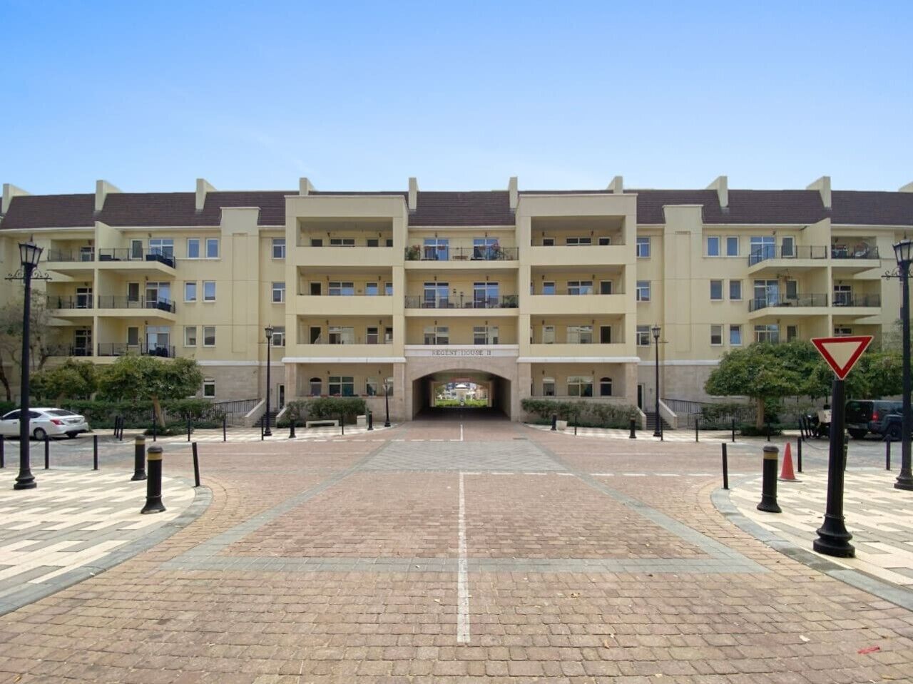 L’entrée d’un hôtel à plusieurs étages, dotée d’une arche centrale, d’une allée pavée et de bornes de protection.
