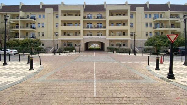 Entrada de un hotel de varios pisos con un arco central, un camino pavimentado y bolardos.