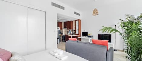 Habitación de hotel moderna con cama, sofá, televisión, zona de comedor y una planta en maceta.