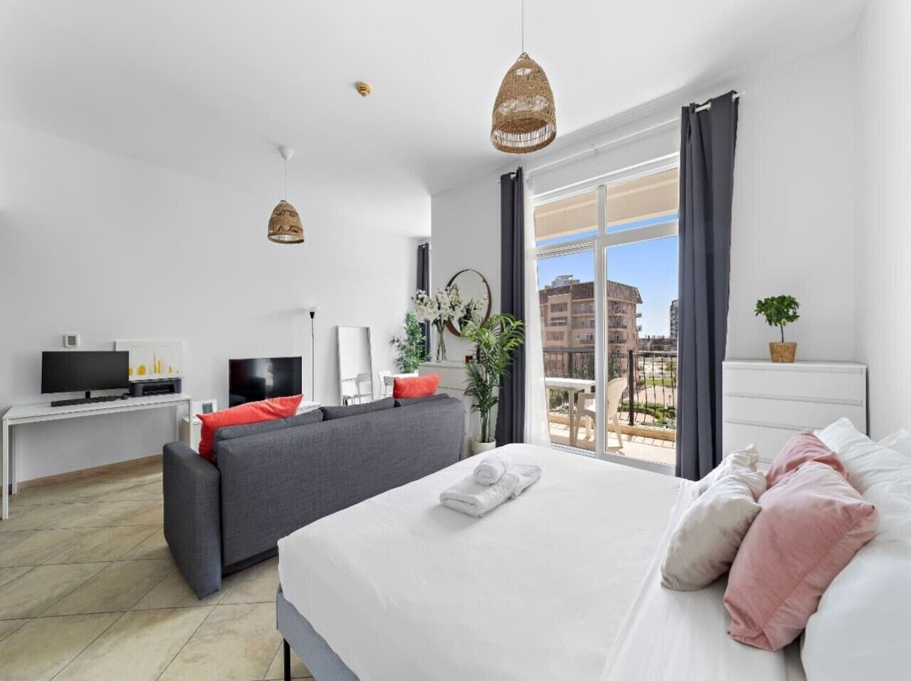 Moderni hotellihuone, jossa on suuri sänky, sohva, televisio ja parveke, jolta on näkymä kaupunkiin.
