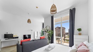 Habitación de hotel moderna con una cama grande, un sofá, un televisor y un balcón con vistas a la ciudad.