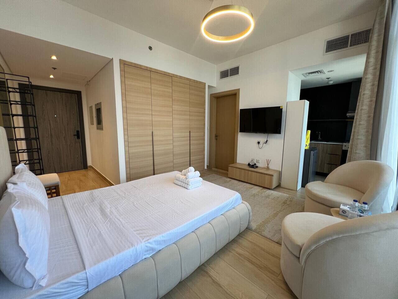 A modern hotel room with a large bed, a seating area, a TV, and a wardrobe.