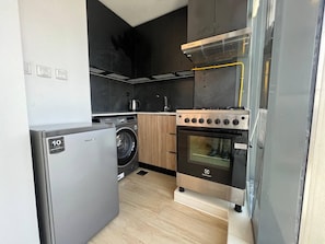 A compact kitchen with a washing machine, oven, and a small countertop. - Chic & Cozy Studio in JVC | Top Amenities & Views! (Dubai)