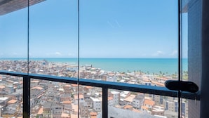 A cityscape with a view of the sea through a window, buildings, and a clear sky. - Apartment w/ sea View in Building w/ Pool Edf1303 (Salvador)
