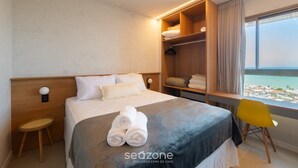 A hotel room with a bed, a desk, a chair, and a view of the sea. - Apartment w/ sea View in Building w/ Pool Edf1303 (Salvador)