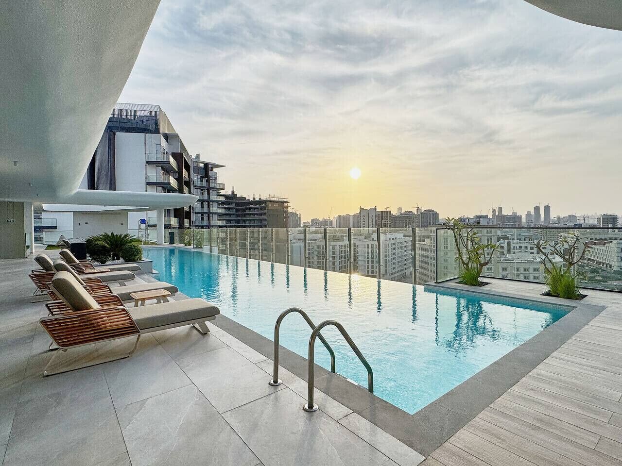 A rooftop infinity pool with lounge chairs and a city skyline view.