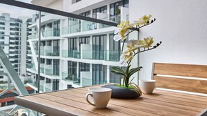 A balcony with a wooden table, two white cups, and a potted orchid plant. - Modern Studio | Rooftop Infinity Pool | Arjan (Dubai)