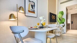 A modern dining area with a white table, two chairs, a framed artwork, and a wall-mounted light fixture. - Modern Studio | Rooftop Infinity Pool | Arjan (Dubai)