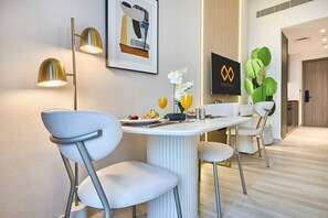 A modern dining area with a white table, two chairs, a framed artwork, and a wall-mounted light fixture. - Modern Studio | Rooftop Infinity Pool | Arjan (Dubai)