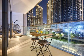 Een balkon met een tafel en stoelen, een hangstoel en een uitzicht op hoge gebouwen 's nachts.