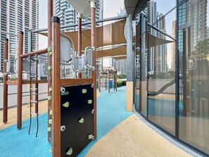 A children's play area with climbing structures and soft play flooring, surrounded by high-rise buildings. - Premium 1BR in Grande | Heart of Downtown Dubai (Dubai)
