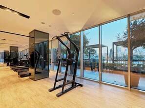 Ein Fitnessraum mit Laufbändern und Kraftgeräten, großen Fenstern und Blick auf eine Stadtlandschaft.
